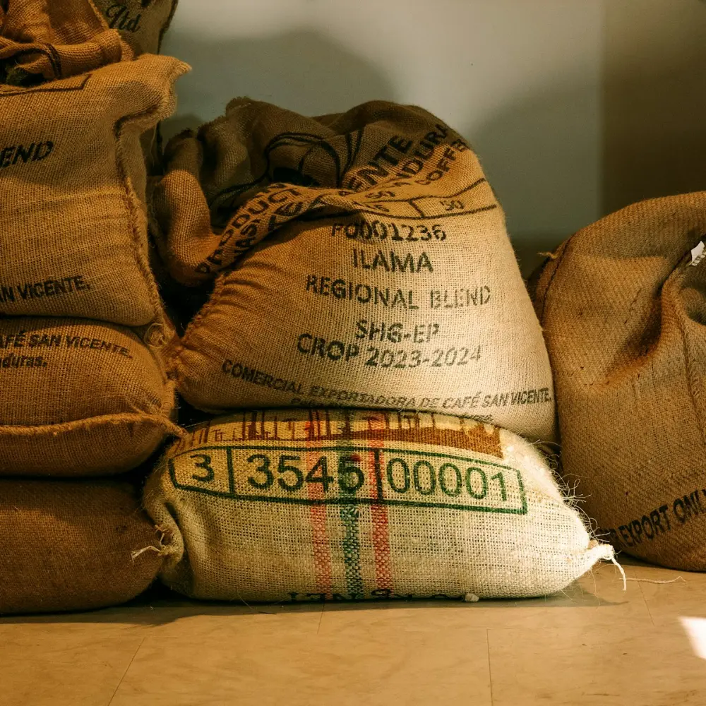 Stacked hessian sacks of green coffee in the roastery, labelled with their origin and crop year